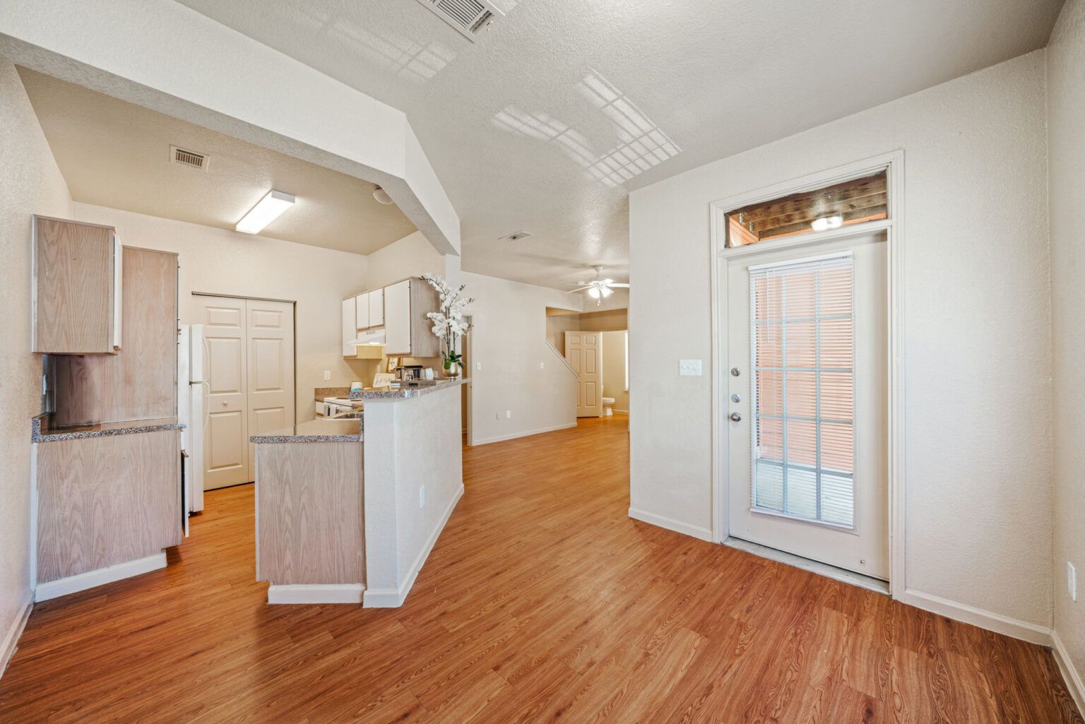 Empty modern kitchen and dining area with light wood floors, white walls, and a sliding glass door.