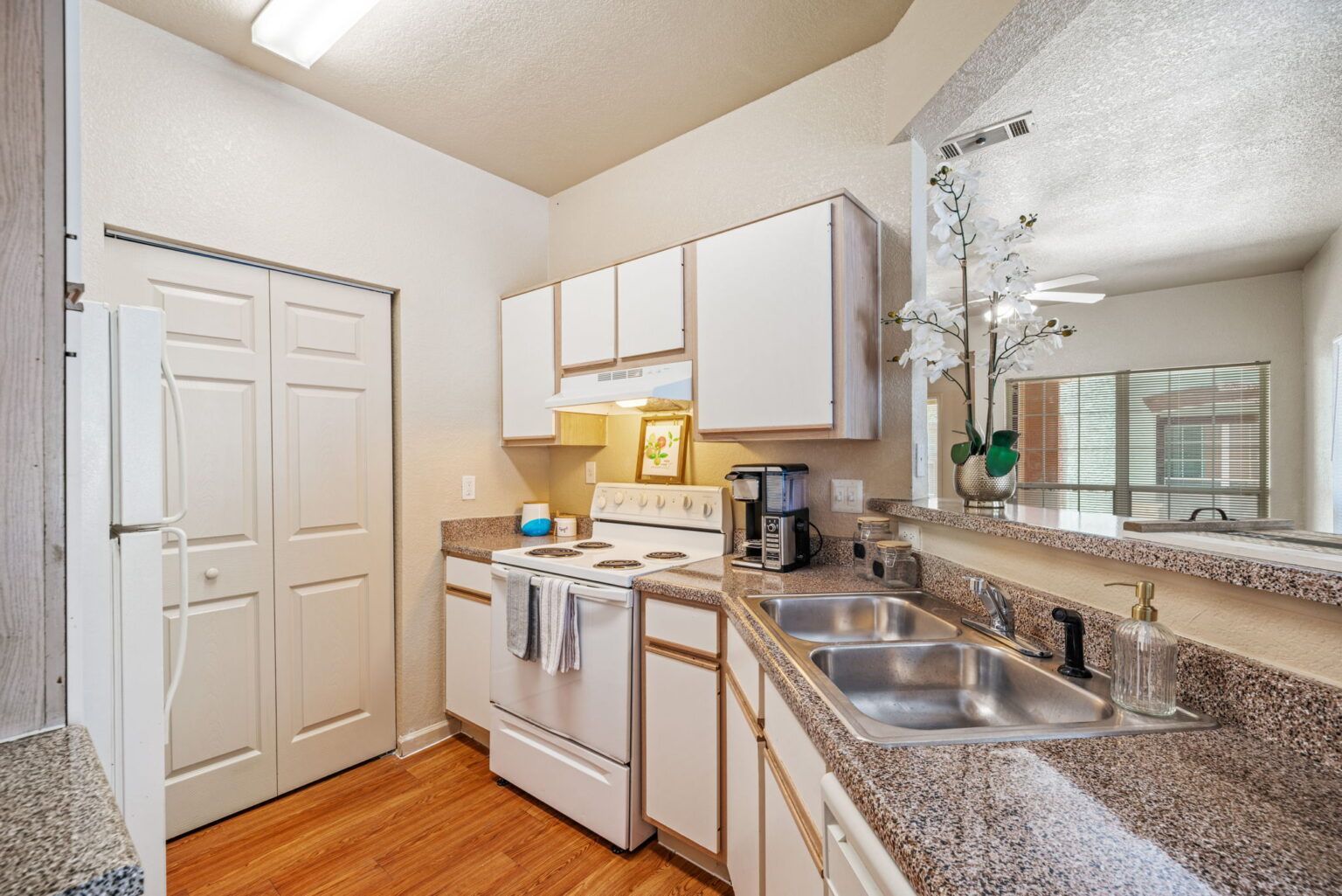 Bright kitchen with white cabinets, granite counters, stove, sink, and wood floor