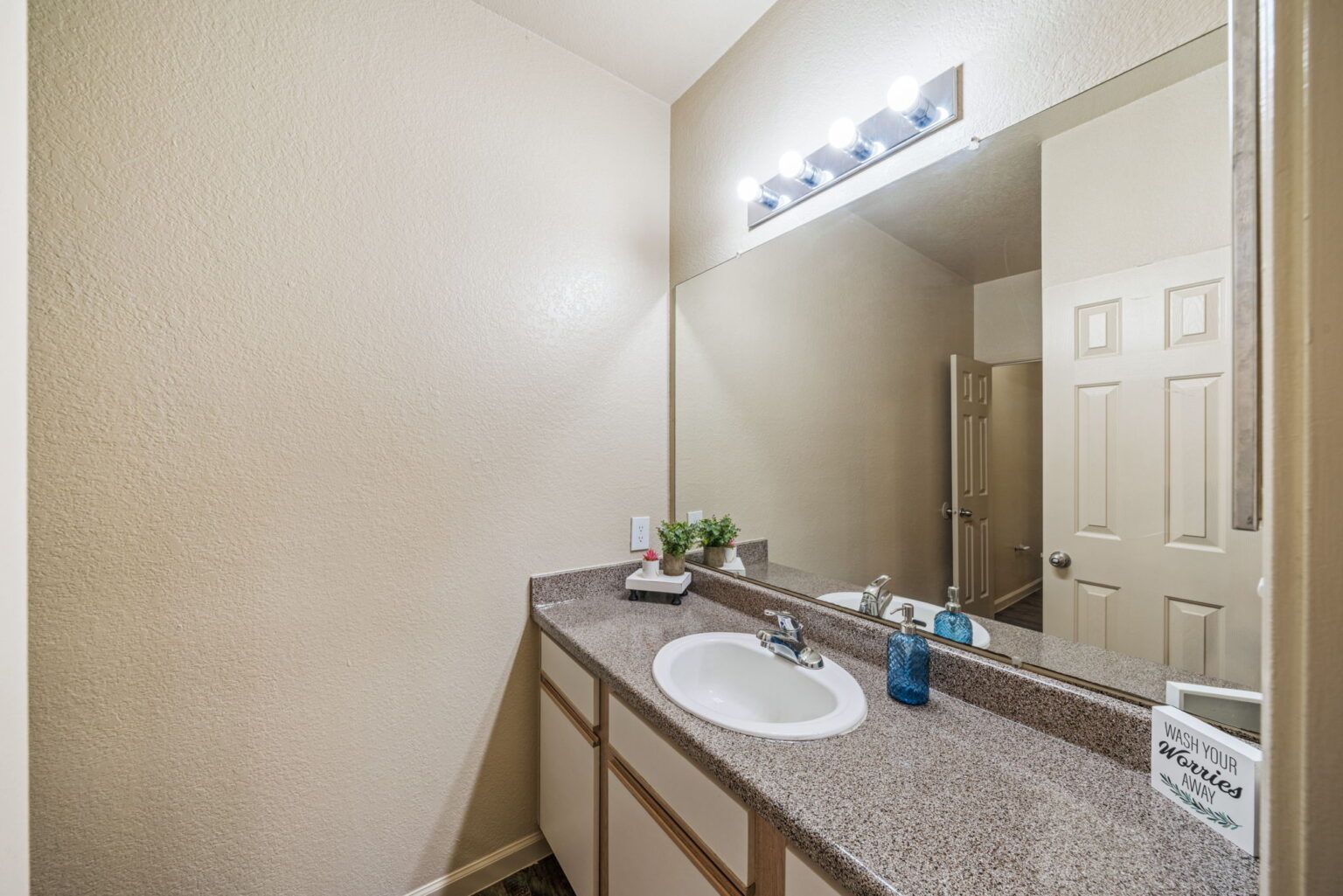 Bathroom vanity with granite countertop, large mirror, and wall-mounted lights in a beige interior.