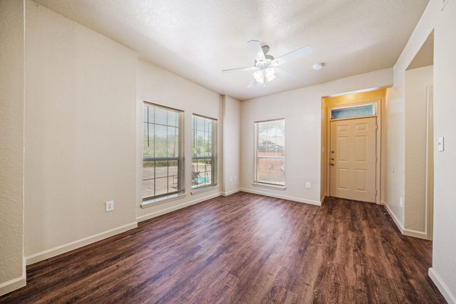 Empty bedroom with wood floors, beige walls, windows, and a ceiling fan-lit light fixture