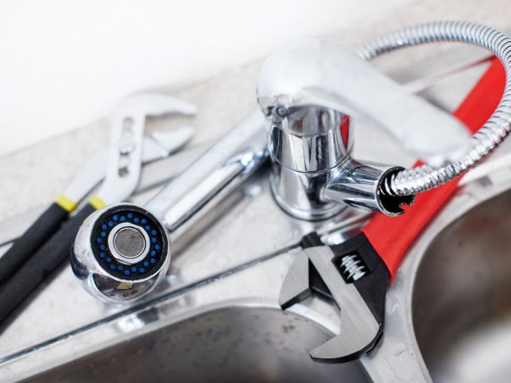 Chrome kitchen faucet with pull-out spray head over a stainless steel sink, hose visible