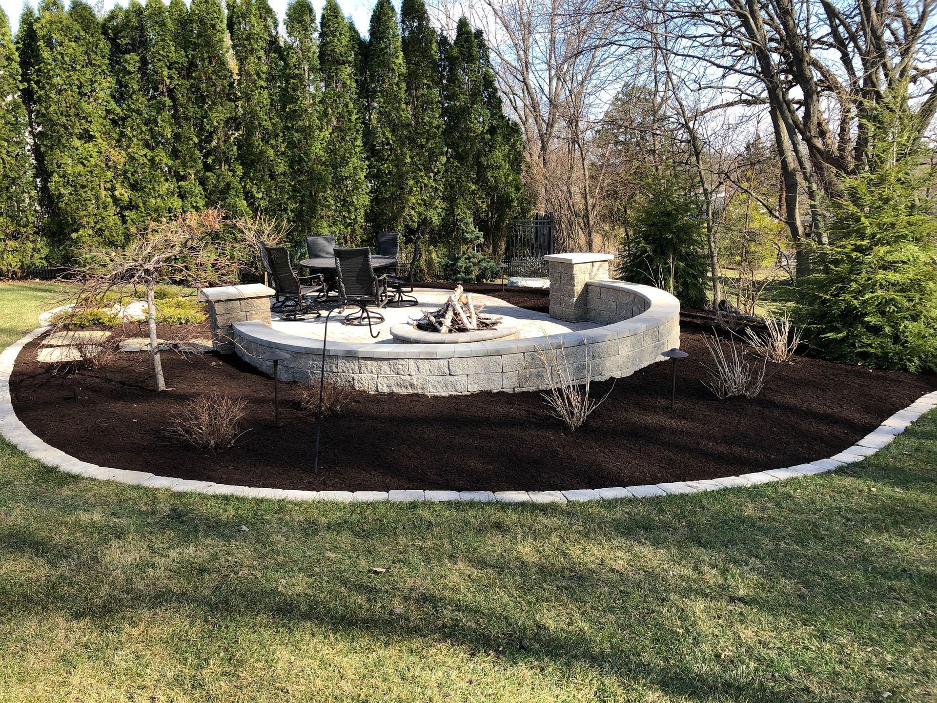 Stone fire pit with seating area, surrounded by mulch and greenery.
