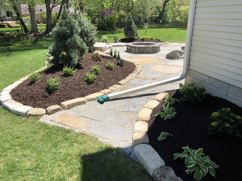 Stone patio and landscaped garden with a fire pit, bordered by stone and mulch.