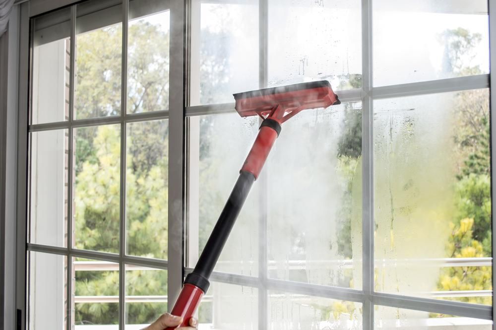 A Person is Cleaning a Window With a Steam Cleaner — South Pacific Cleaning in Bentley Park, QLD