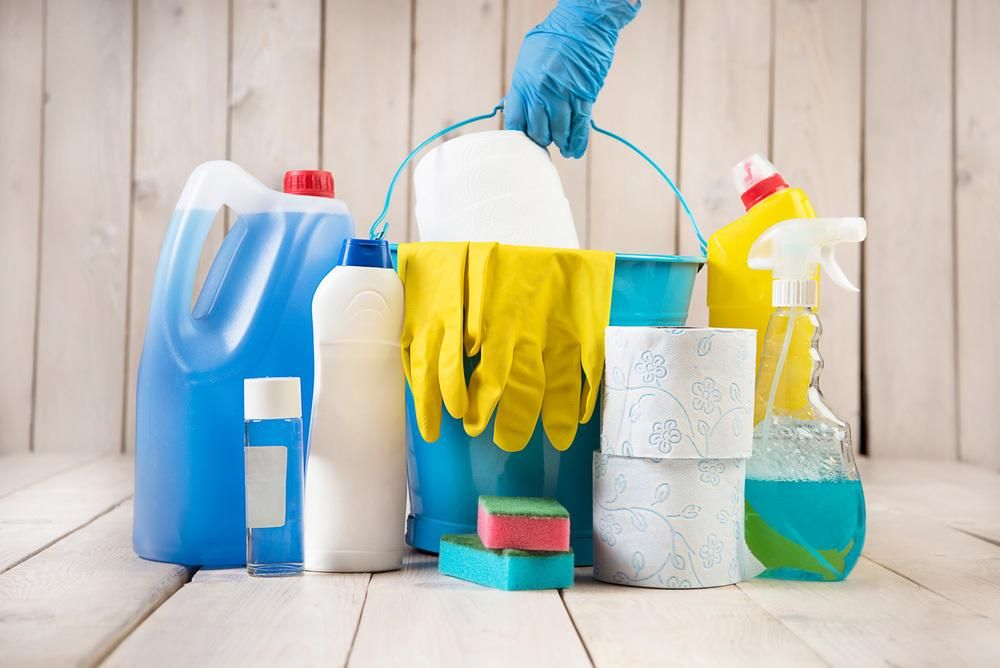 A Person is Holding a Bucket of Cleaning Supplies on a Wooden Table — South Pacific Cleaning in Bentley Park, QLD