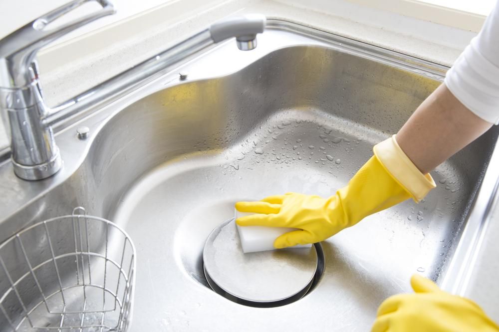 A Person Wearing Yellow Gloves is Cleaning a Stainless Steel Sink With a Sponge — South Pacific Cleaning in Cairns City, QLD