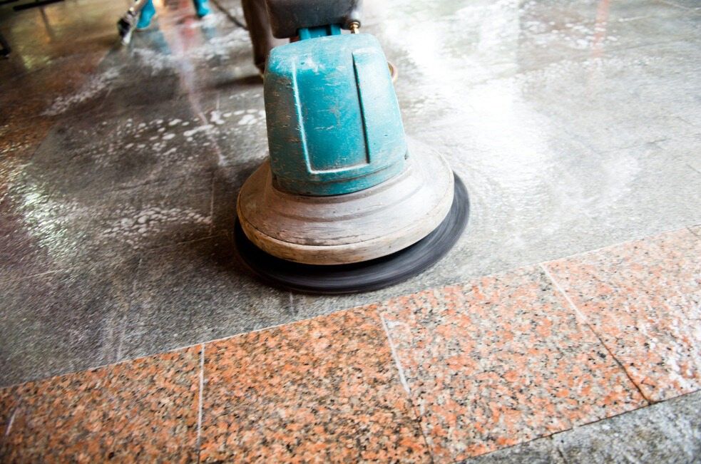 A Person is Cleaning a Granite Floor With a Machine — South Pacific Cleaning in Cairns City, QLD