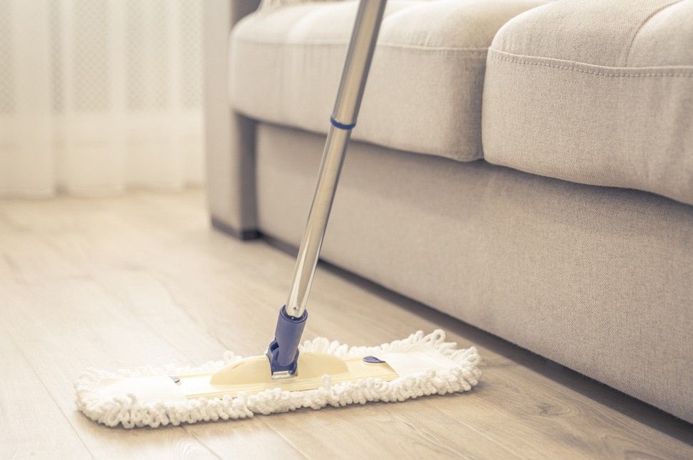 A Mop is Sitting on a Wooden Floor Next to a Couch — South Pacific Cleaning in Cairns City, QLD