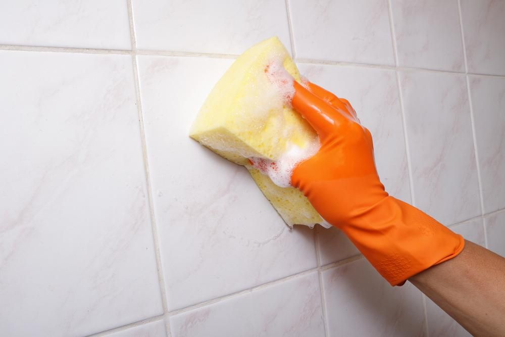 A Person Wearing Orange Gloves is Cleaning a Tile Wall With a Sponge — South Pacific Cleaning in Edmonton, QLD
