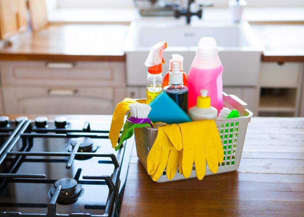 A Basket of Cleaning Supplies is Sitting on a Stove Top in a Kitchen — South Pacific Cleaning in Bentley Park, QLD