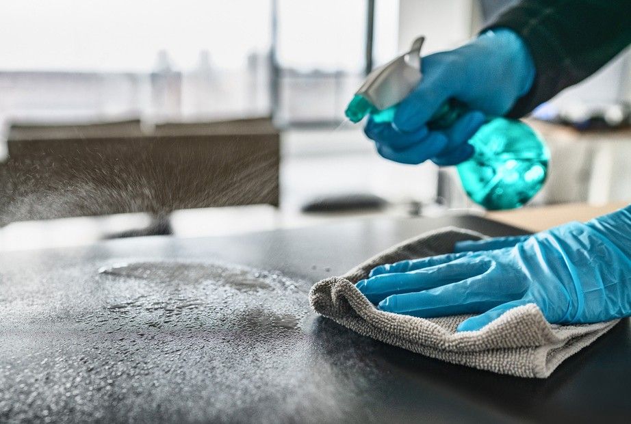 A Person Wearing Blue Gloves is Cleaning a Counter With a Cloth and Spray Bottle — South Pacific Cleaning in Redlynch, QLD