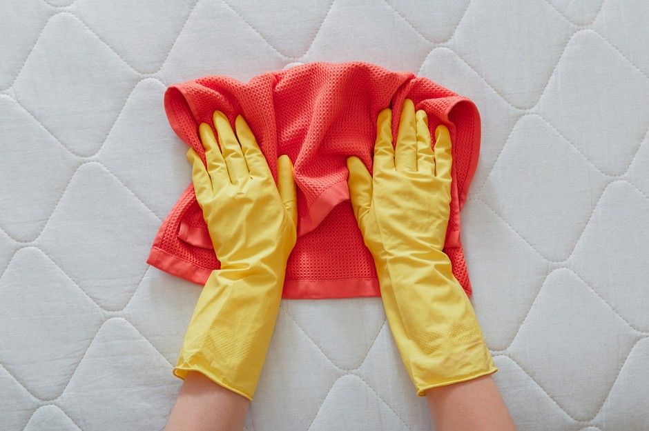 A Person Wearing Yellow Gloves is Cleaning a Mattress With a Towel — South Pacific Cleaning in Smithfield, QLD
