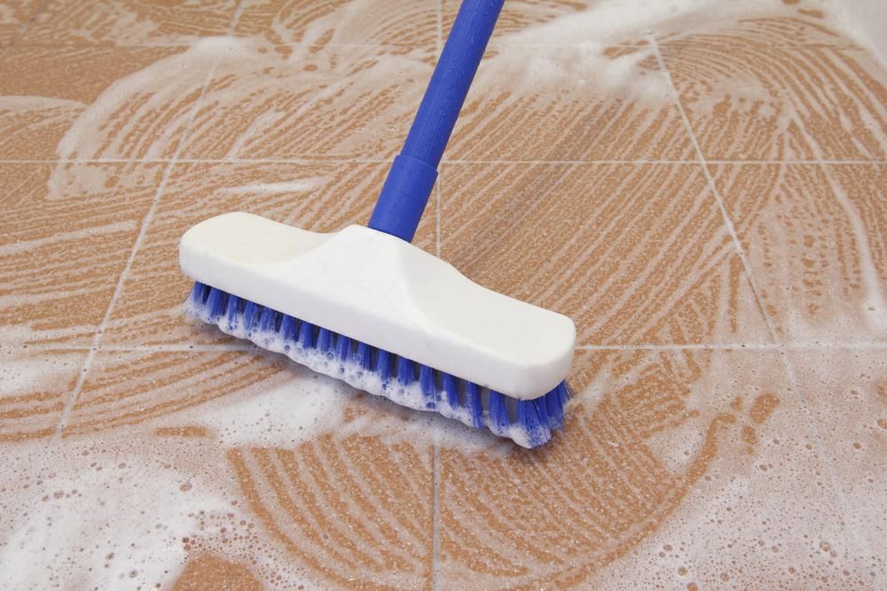 A Blue and White Brush is Cleaning a Tiled Floor — South Pacific Cleaning in Smithfield, QLD