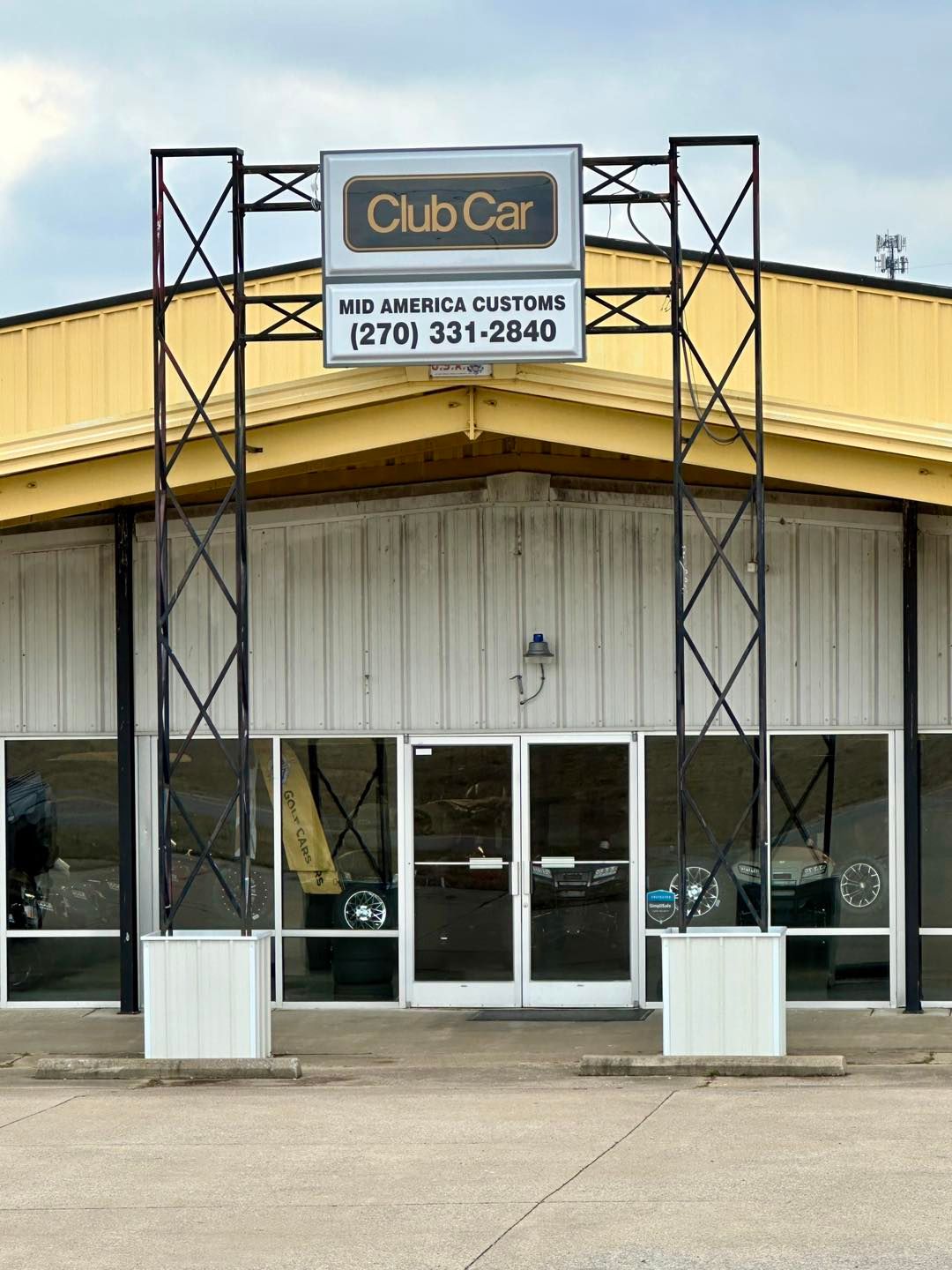 Club Car sign over building entrance, white doors and windows. Black metal supports, yellow and white facade.