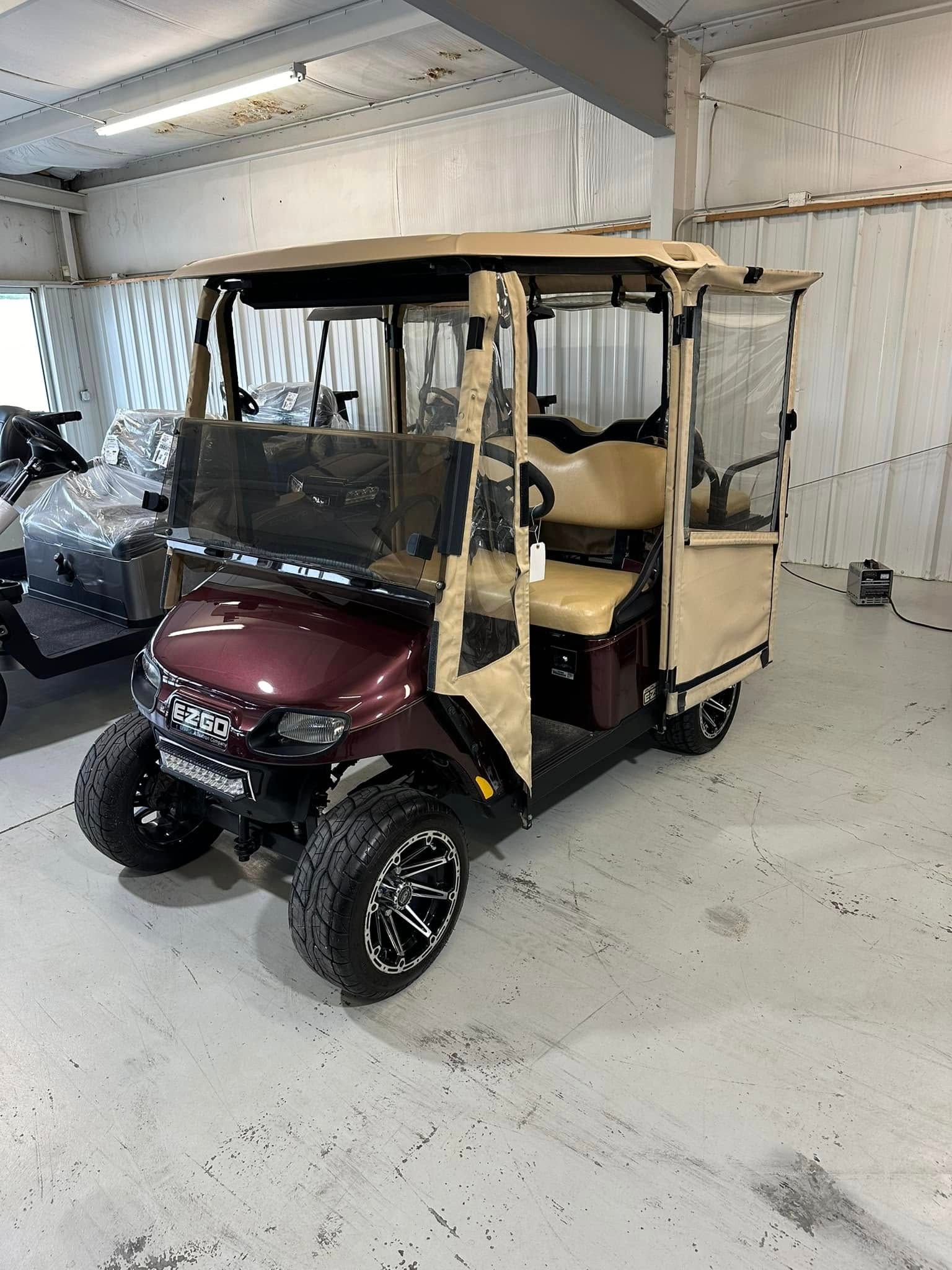 Burgundy golf cart with tan roof and enclosure; parked inside.
