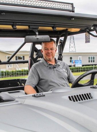 Man in grey shirt driving a gray off-road vehicle with a light bar.