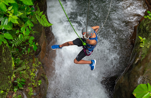A man is jumping over a waterfall with a rope.