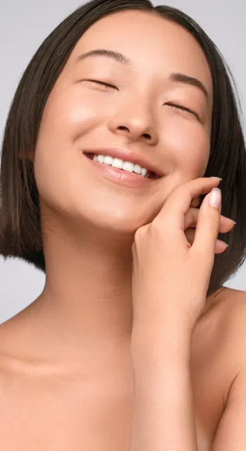 Woman with reddish hair and freckles smiles, touching her face.