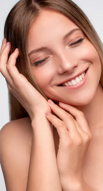 Woman with closed eyes, smiling broadly, hand on cheek. Skin glowing.