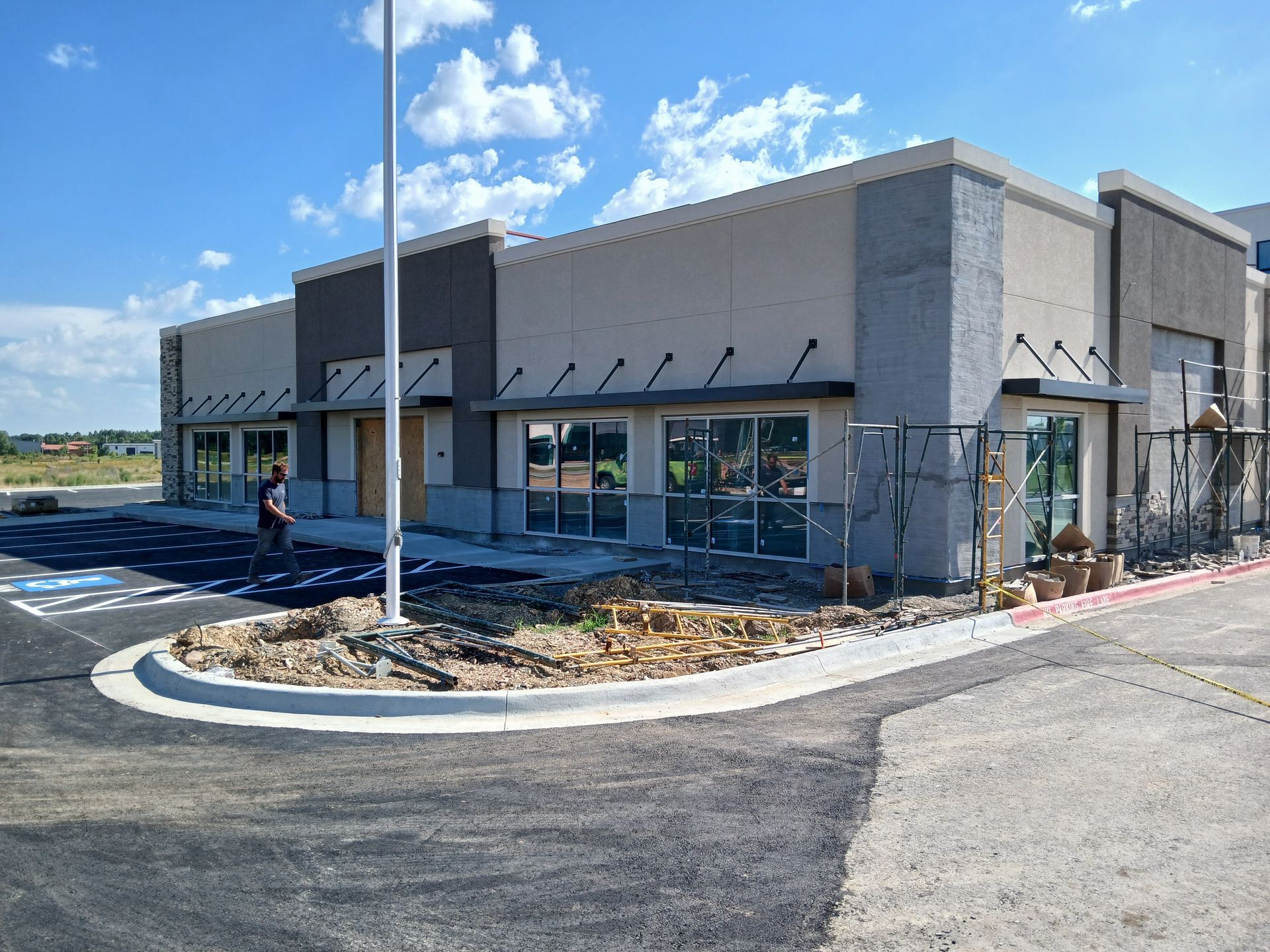 Modern commercial building exterior with gray walls, glass doors, awnings, and a curved driveway under a blue sky