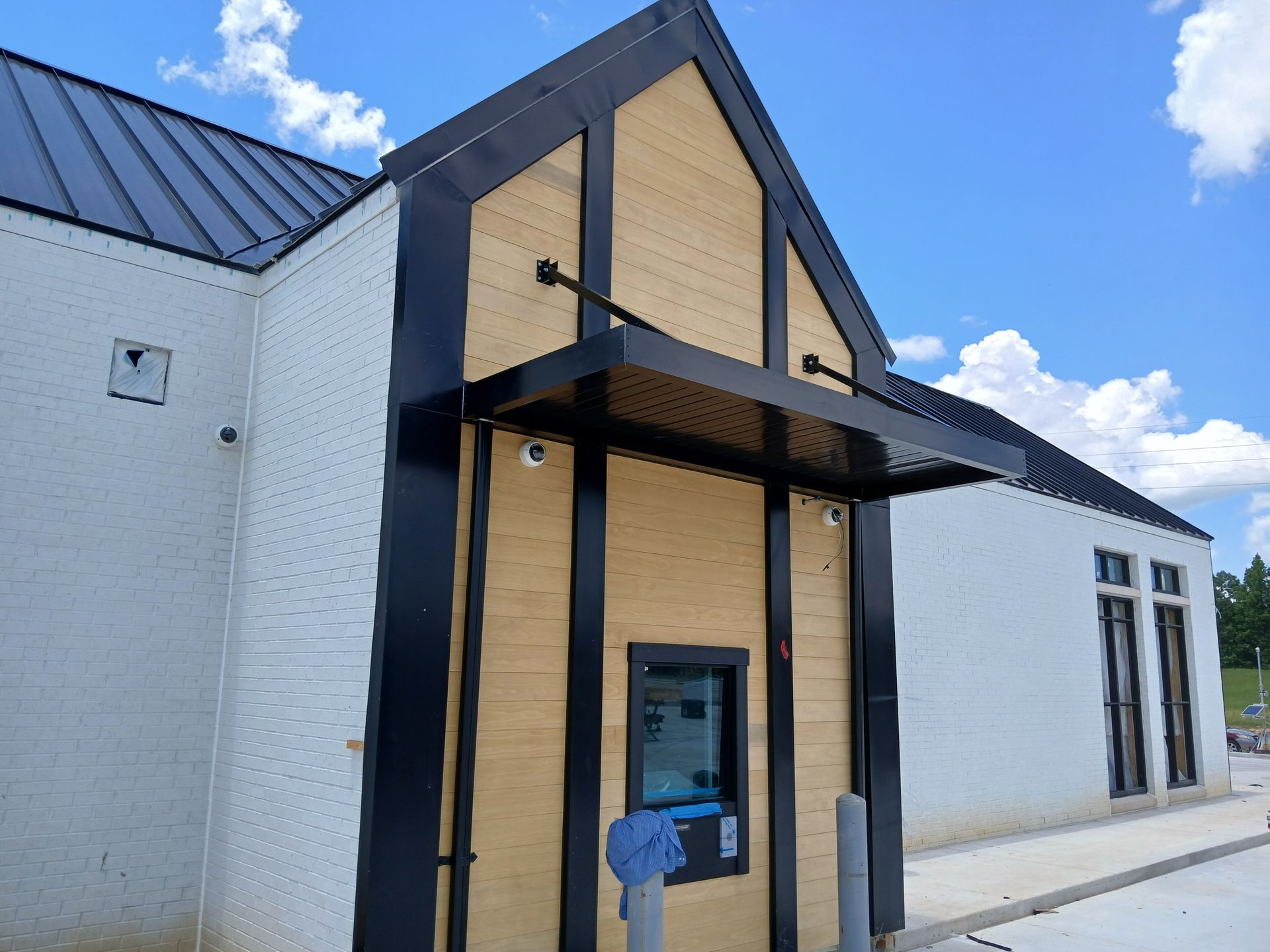 Small entrance with a black awning and beige siding on a white brick building under a blue sky.
