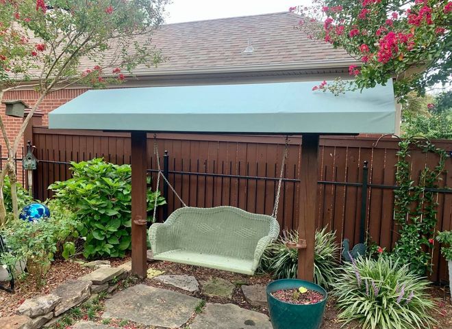 A swing is sitting under a canopy in a backyard next to a fence.