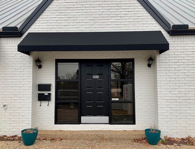 A white brick house with a black door and awning.