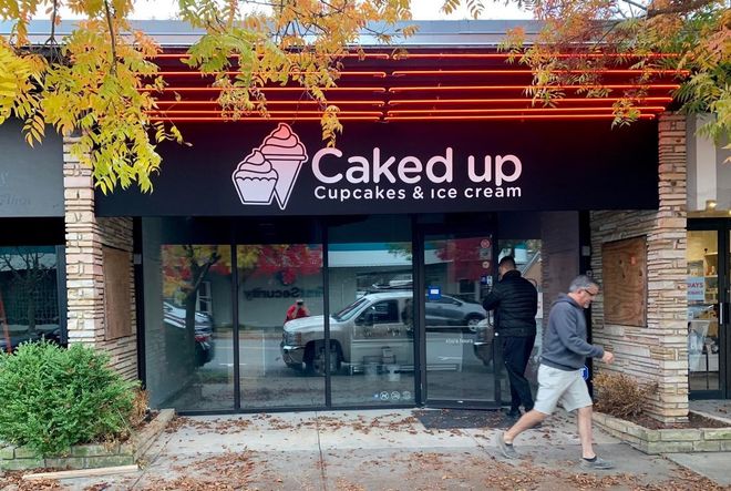 A man is walking in front of a caked up cupcakes and ice cream store.