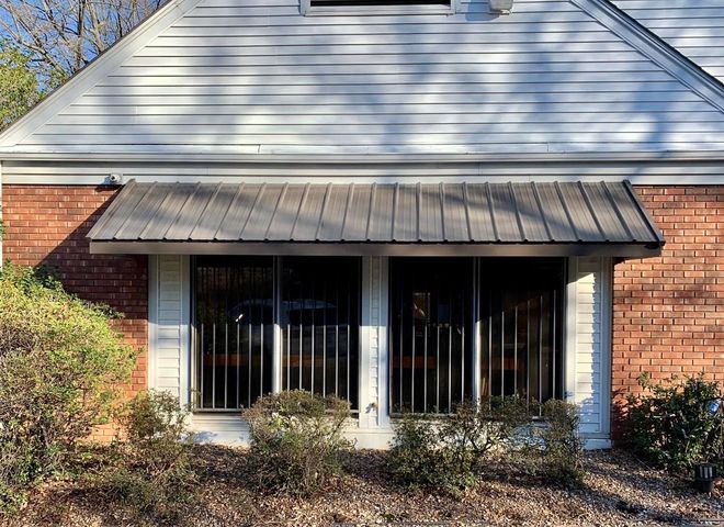 A white house with a brick wall and a metal awning over the windows.