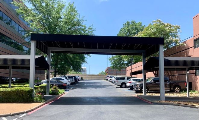 A parking lot with cars parked under a canopy in front of a building.