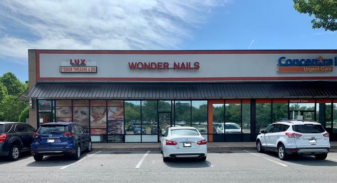 A row of cars are parked in front of a store called wonder nails.