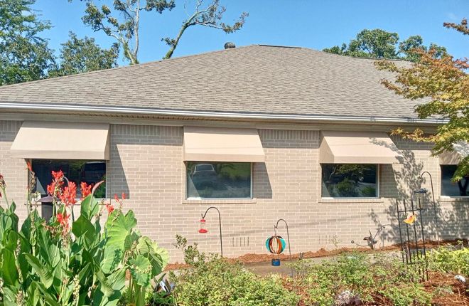 A brick house with awnings on the windows and a garden in front of it.