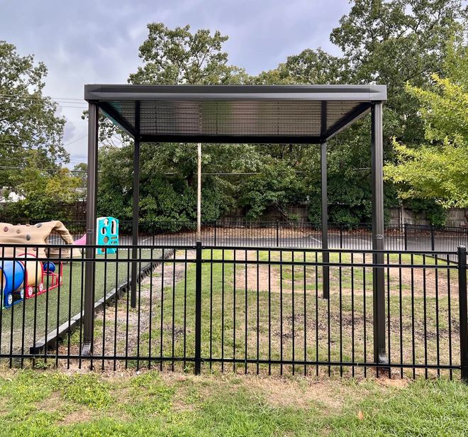 A black fence surrounds a playground in a backyard.