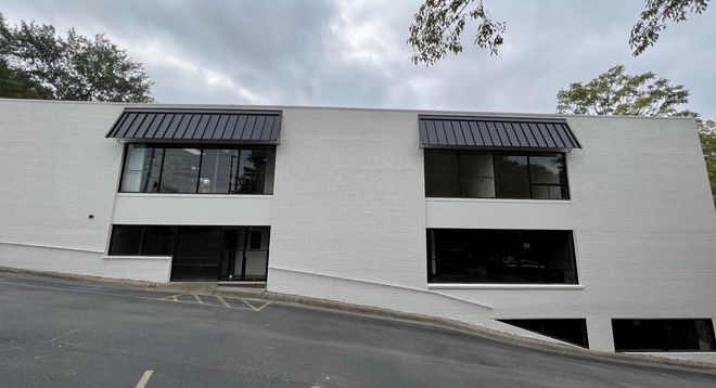 A large white building with a black roof is sitting on top of a hill.