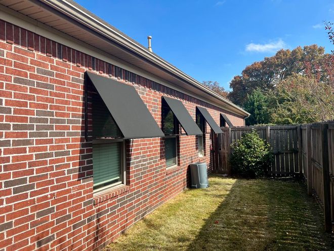 A brick house with awnings on the windows and a fence in the backyard.