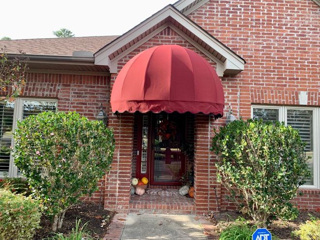 A brick house with a red awning over the front door.