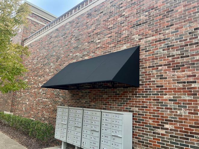 A brick wall with a black awning over a row of mailboxes.