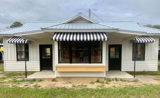 A white house with black and white awnings on the porch.