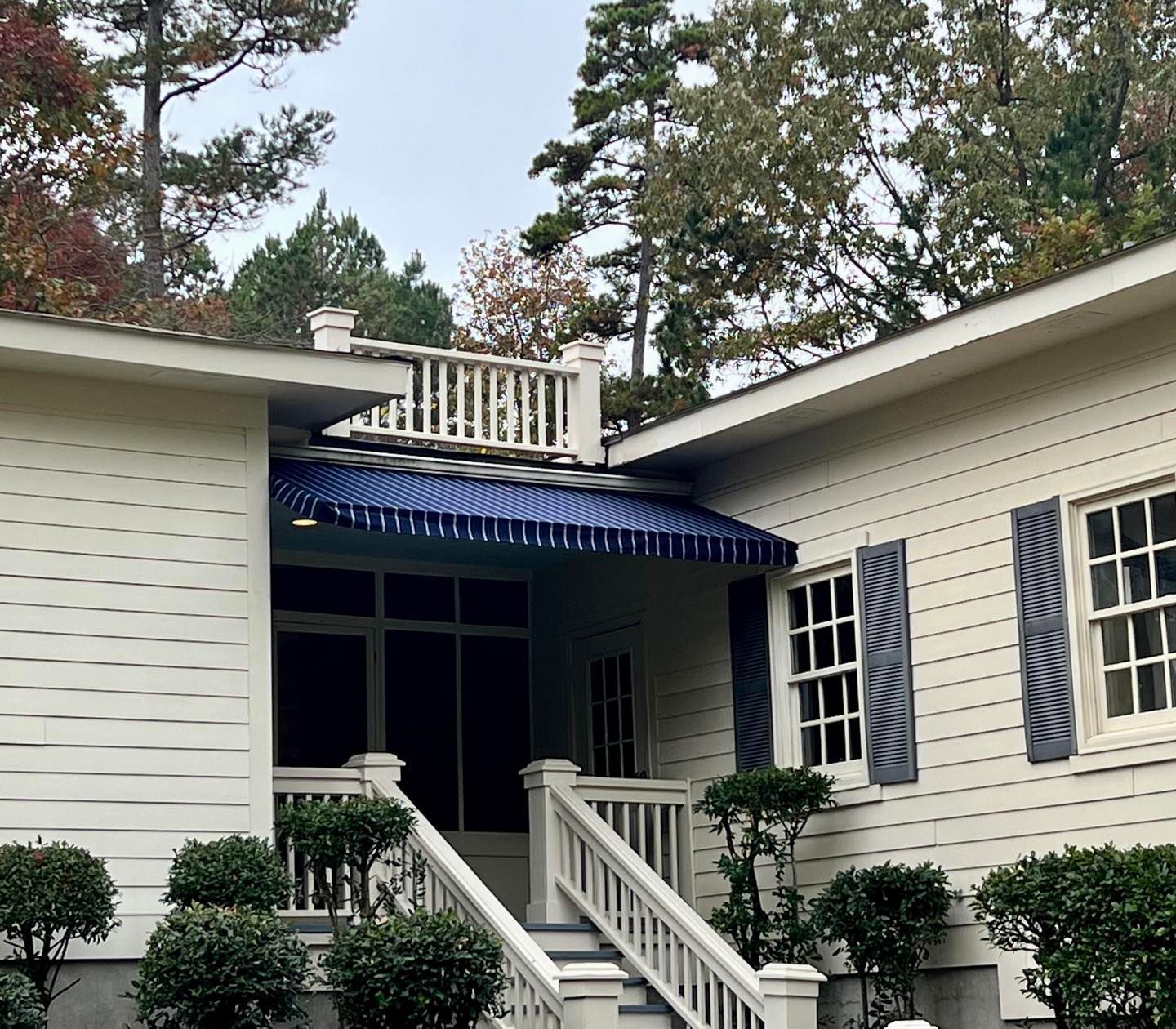 A white house with blue shutters and a blue awning