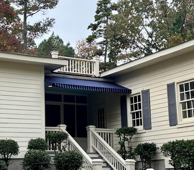 A white house with blue shutters and a blue awning