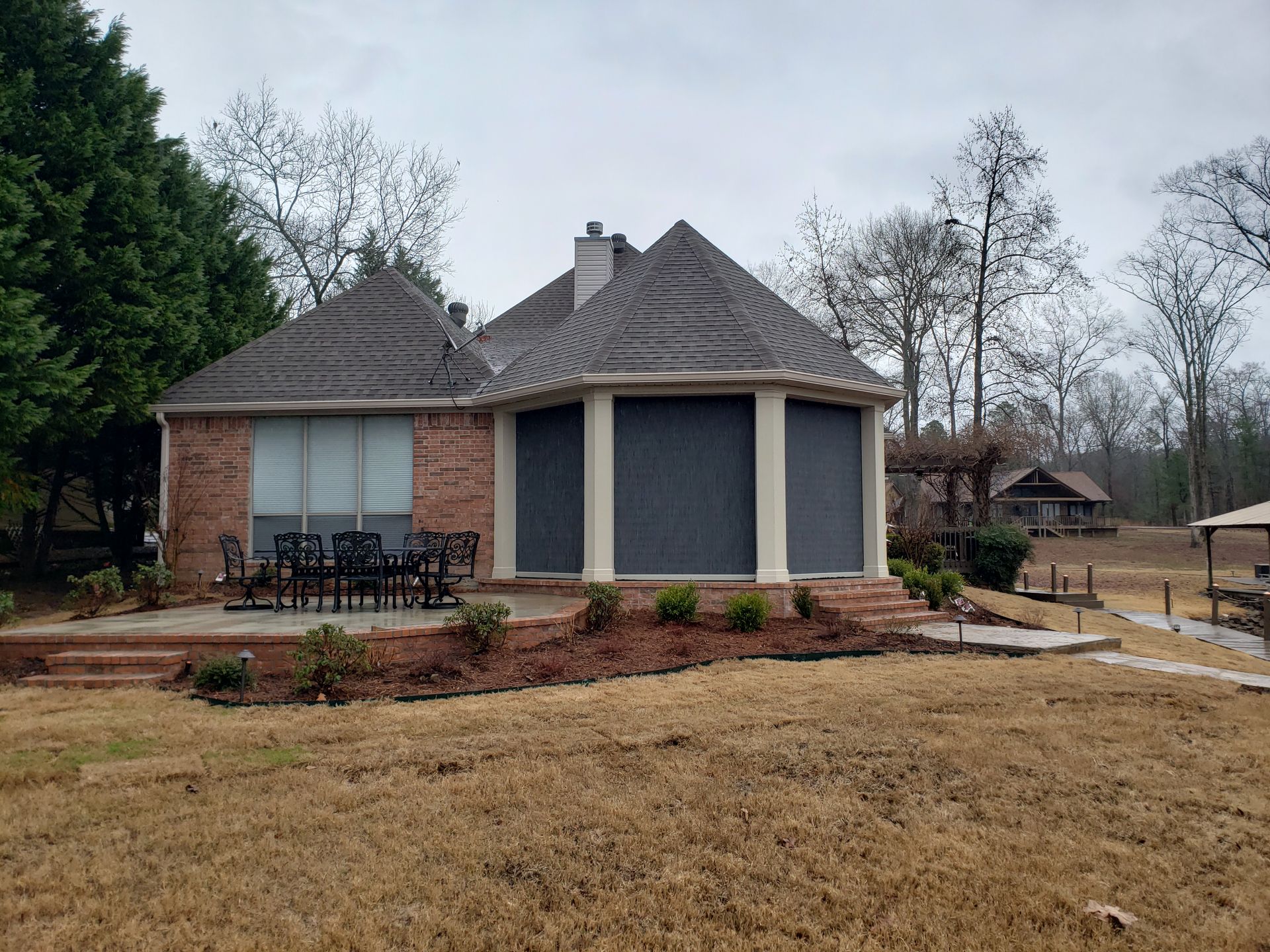 Brick house with gray roof and screened porch in a leafless suburban yard