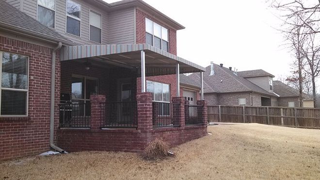 A large brick house with a covered porch and a fence in the backyard.