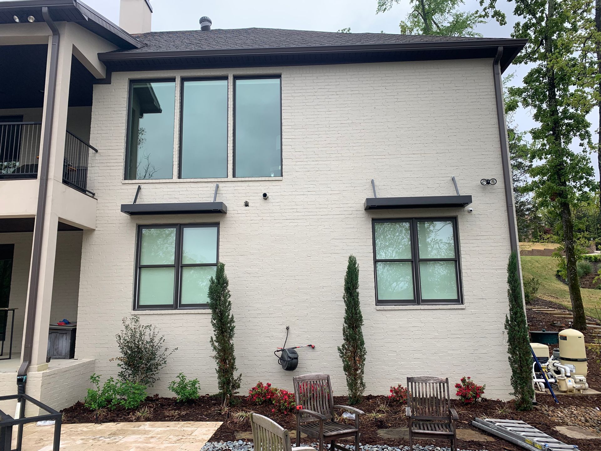 Two-story white brick house with black trim, large windows, and a small front garden with chairs.
