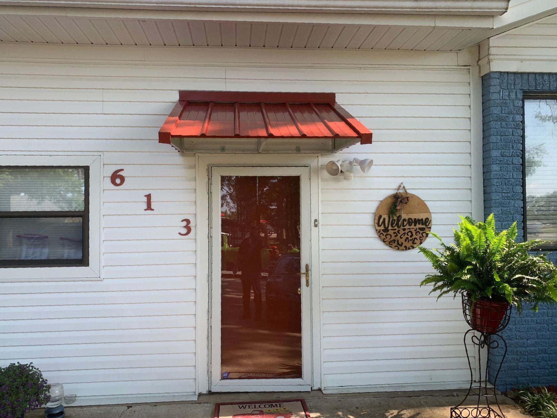 Front entrance with white siding, red awning, glass door, house number 613, and a potted plant.
