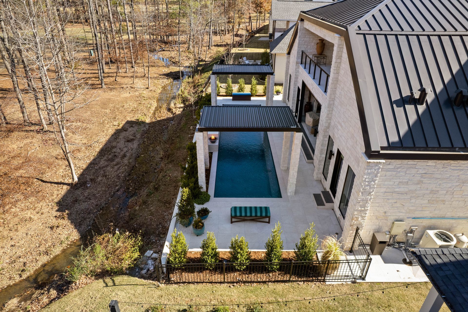 Aerial view of a modern house patio with blue awning, seating, and landscaped yard beside a wooded area