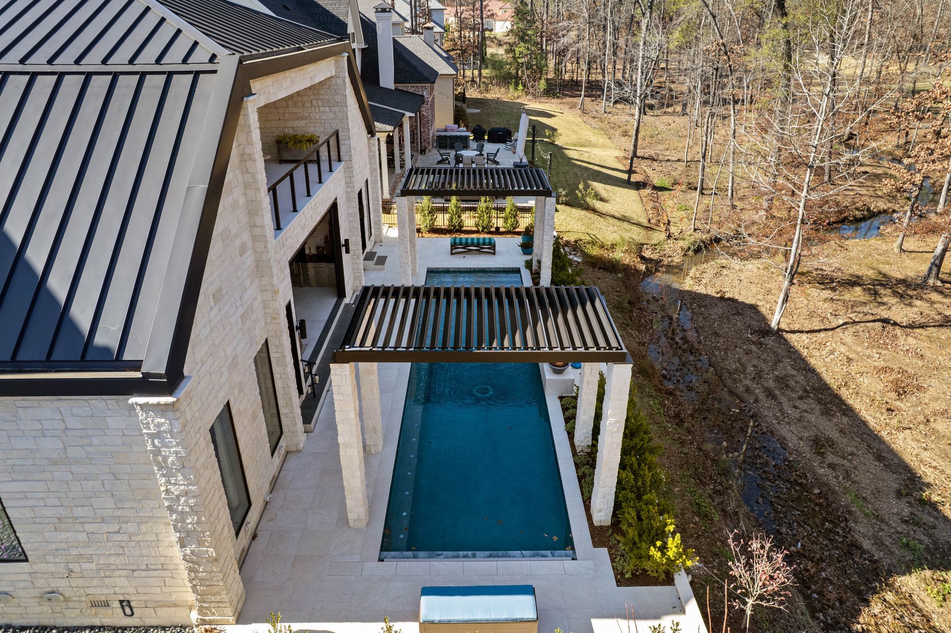 Modern house patio with a turquoise pool and black pergola beside a wooded backyard