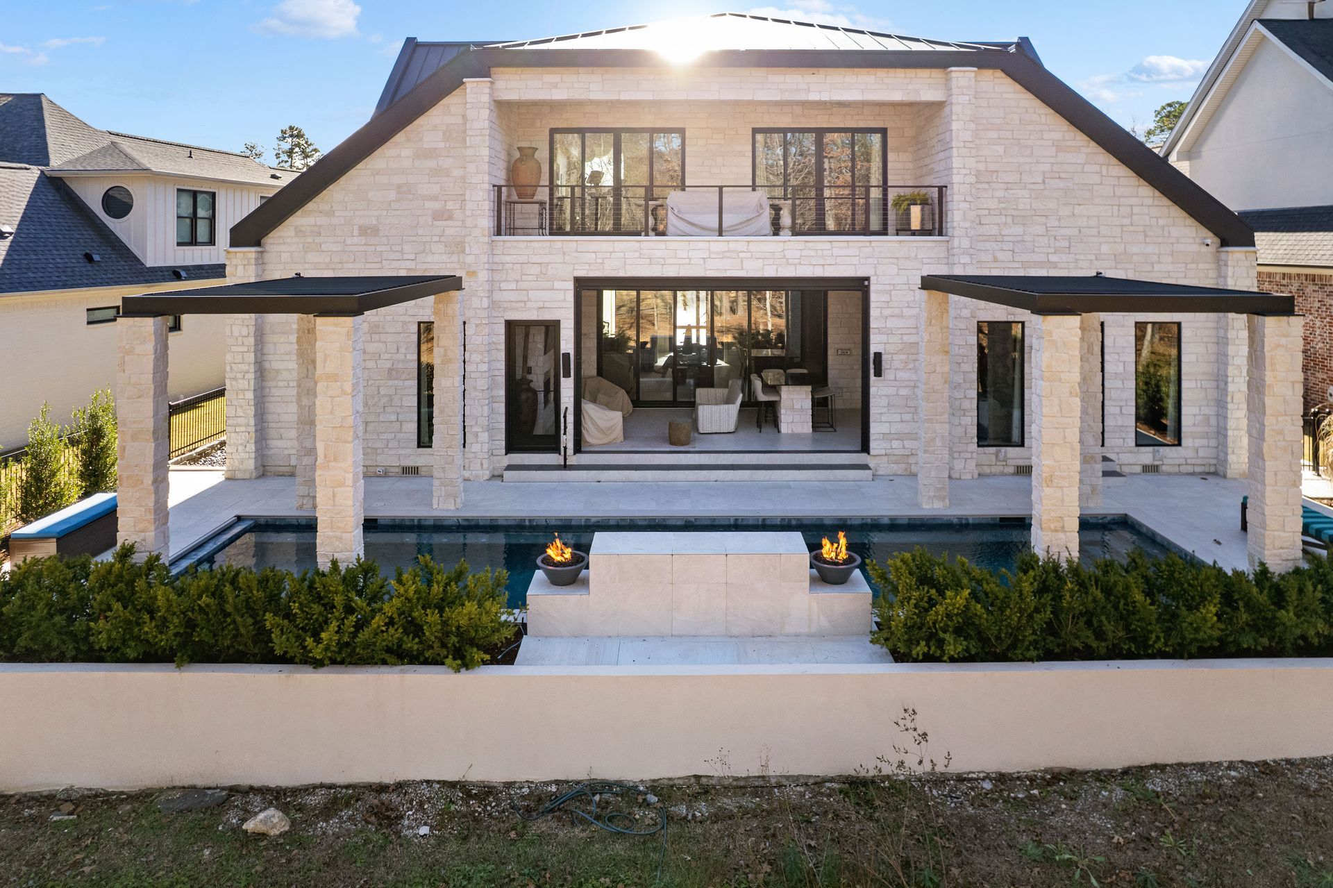 Modern two-story stone house with a front patio, glass doors, and neatly landscaped entryway