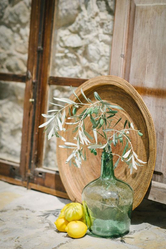 Glass vase with white flowers beside lemons and a woven hat on a rustic floor