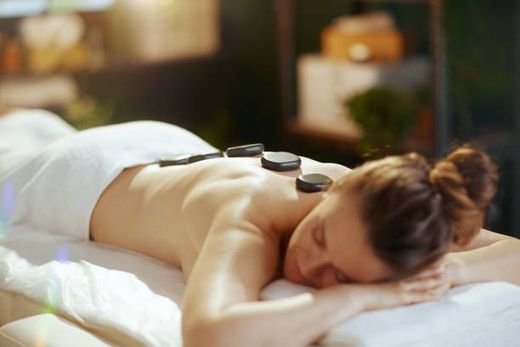 A woman is laying on a massage table with rocks on her back.