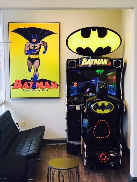 Batman-themed arcade game room with yellow wall art, a pinball machine, and a Batman sign